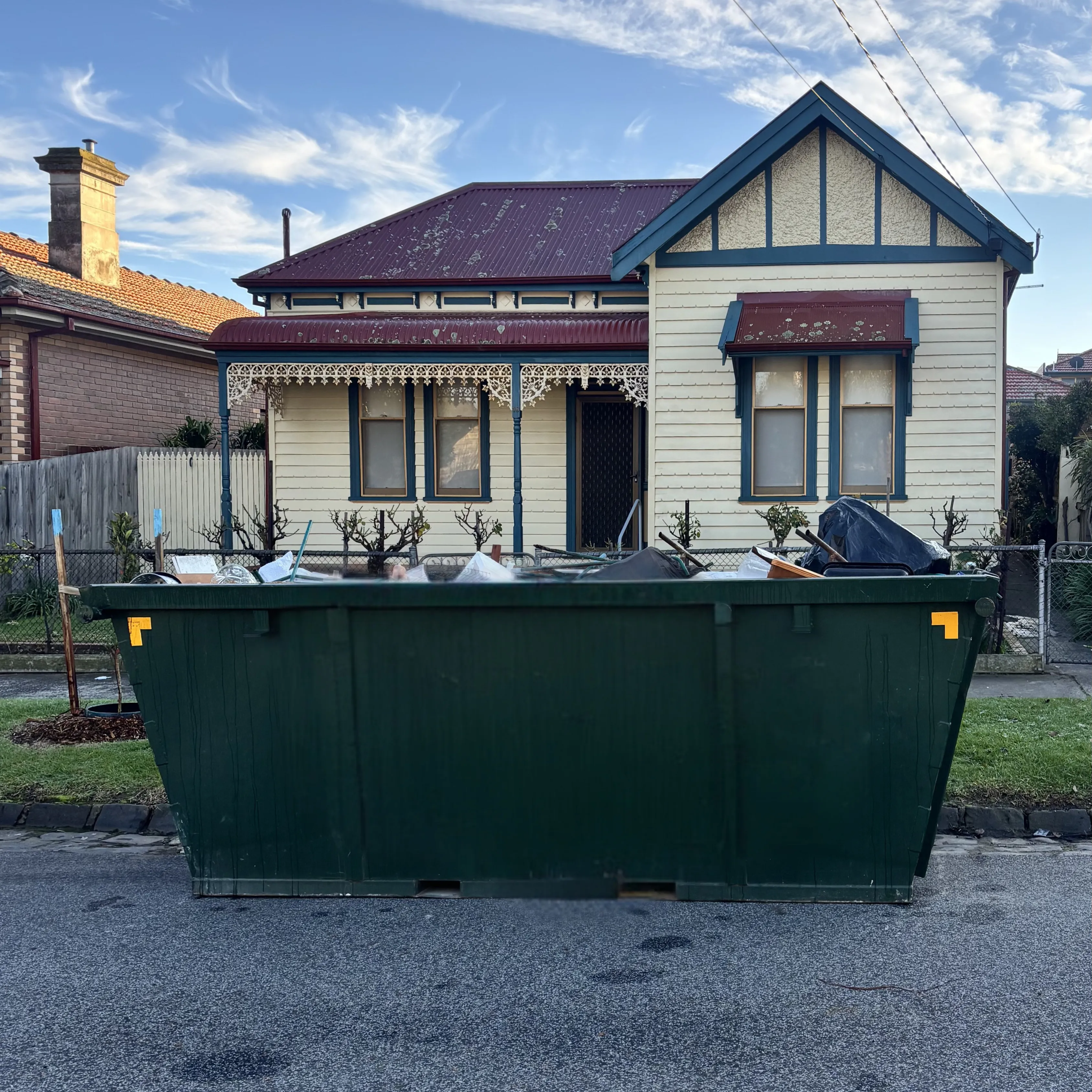 A 4 cubic metre skip on the kerb outside a weatherboard cottage in Brunswick, filled with household waste